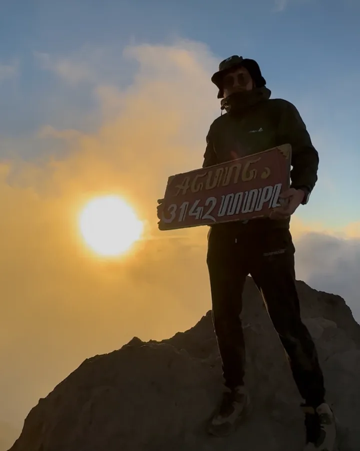 Anthony at sunrise on the summit of Mount Agung, holding the summit sign